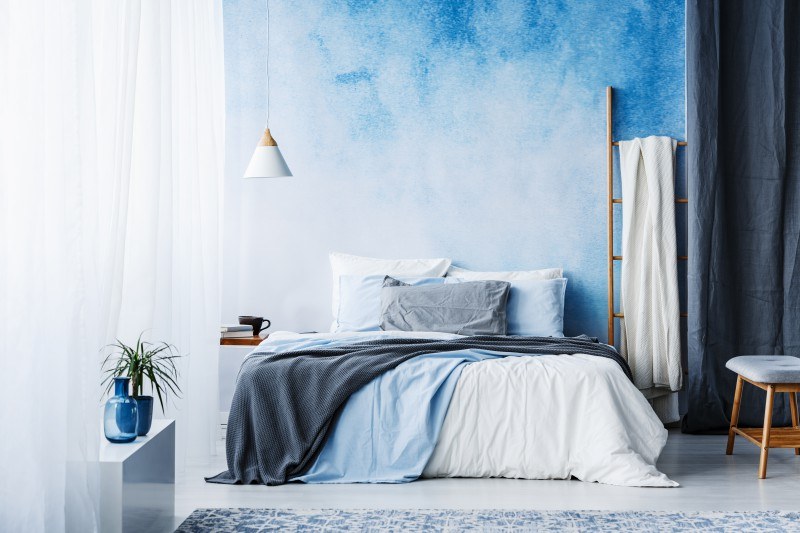 Canva Grey and blue bedding on bed in spacious bedroom interior with ladder and plant